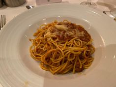 a white plate topped with spaghetti and sauce on top of a table next to silverware