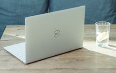 a laptop computer sitting on top of a wooden table next to a glass of water