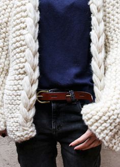 a person wearing a white knitted cardigan and black jeans with a brown belt