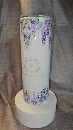 a white and purple flowered glass sitting on top of a white stand in front of a gray background