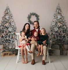 a man and woman sitting on a chair with two children in front of christmas trees