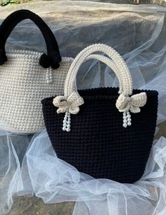 two crocheted purses sitting on top of a white and black cloth bag