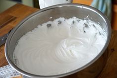 a metal bowl filled with white frosting on top of a wooden table