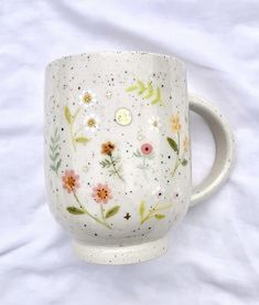 a white coffee cup with flowers painted on the outside and inside, sitting on a bed sheet