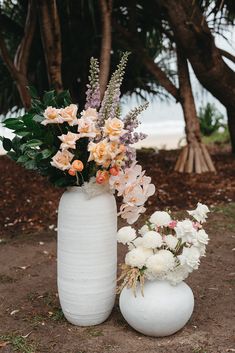 two white vases with flowers in them sitting on the ground next to each other