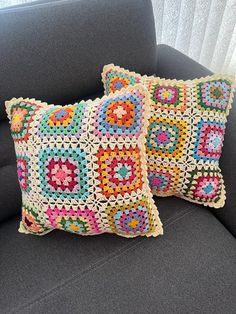 two crocheted pillows sitting on top of a gray couch next to a window