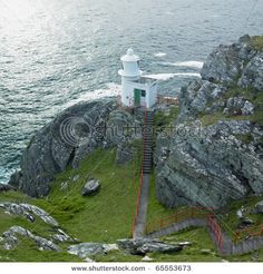 a white lighthouse on top of a rocky cliff next to the ocean with stairs leading up to it