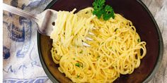 a bowl filled with pasta and parsley on top of a blue towel next to a fork