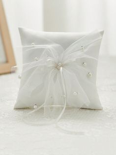 a white ring pillow with pearls and ribbon on the front is sitting on a bed