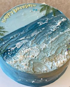 a birthday cake with blue frosting and palm trees on the top is sitting on a table