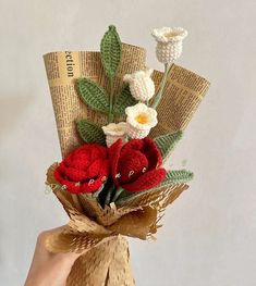 a hand holding a bouquet of crocheted flowers on top of burlap