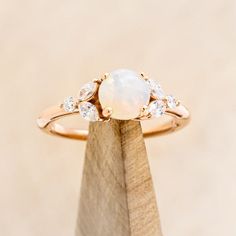 a white opal and diamond ring sitting on top of a wooden stand