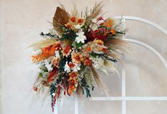 an arrangement of flowers and foliage on a white arch