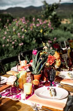 the table is set with flowers and plates for two people to eat on, overlooking mountains