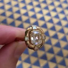 a close up of a person's hand holding a ring with an oval shaped diamond