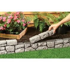 a person is placing plants in a planter on top of a stone wall that has been built into the ground