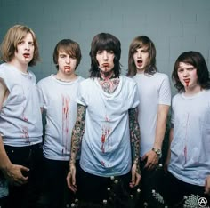 a group of young men standing next to each other in front of a wall with blood all over them