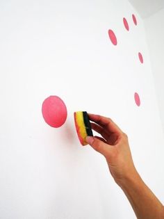 a hand holding a pink and yellow doughnut in front of a white wall with polka dots on it