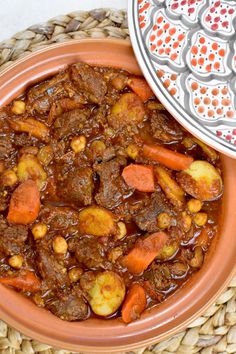 a bowl filled with stew and carrots on top of a woven place mat next to a plate