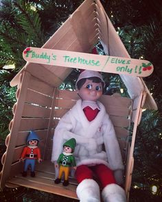 an elf is sitting in a house ornament with two elves on the porch