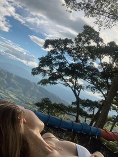 a woman laying in a hammock on top of a mountain overlooking the ocean