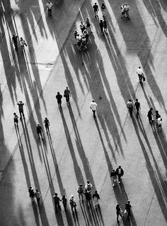 black and white photograph of people walking down the street with their shadows on the ground