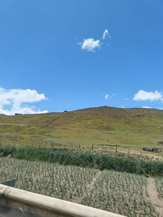 an open field with hills in the background and blue skies above it on a sunny day