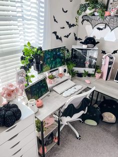 a white desk topped with a computer monitor next to a window filled with plants and bats