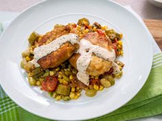 a white plate topped with chicken covered in sauce and corn on the cob next to a green napkin