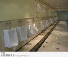 a row of urinals in a bathroom with tile flooring and wall mounted hand dryers