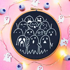 a black and white embroidery pattern on a pink background with halloween decorations around the hoop