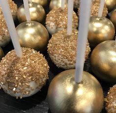 some gold and white cake pops are on a black surface with candles sticking out of them