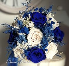 a blue and white bridal bouquet on top of a table with a clock in the background