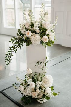 White wooden pillars hold large floral arrangements for a wedding ceremony, with white hydrangeas, white roses, and larkspur, to enhance the class white wedding Floral Urns Wedding Ceremony, Plinth Wedding Flower Arrangements, Outside Wedding Ceremony Flowers, Wedding Altar Arrangements, Floor Arrangements Wedding Ceremony, Pillar Arrangements Wedding, Plinth Flowers Wedding, Ceremony Flowers On Pedestals, Wedding Altar Pillars