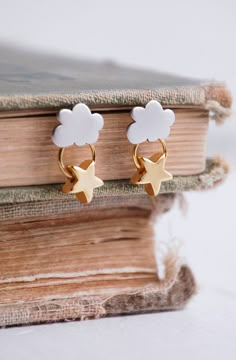 a pair of gold and white earrings sitting on top of a book with clouds in the background