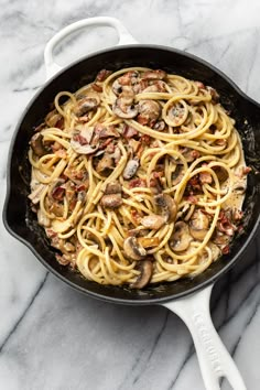 a skillet filled with pasta and mushrooms on top of a marble countertop next to a spatula