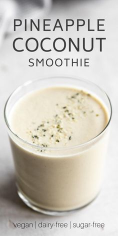 a glass cup filled with pineapple coconut smoothie on top of a white table