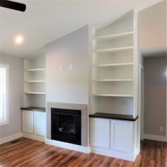 an empty living room with white bookcases and fireplace in the center, surrounded by wood flooring