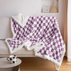 a purple and white checkered blanket sitting on top of a couch next to a cup