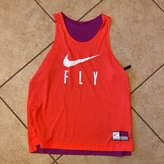 a red tank top with the word fly on it sitting on a tile floor next to a pair of scissors