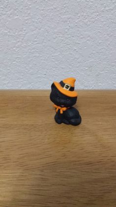 a small black and orange hat sitting on top of a wooden table next to a white wall