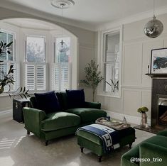 a living room filled with green couches and a fire place in front of a window