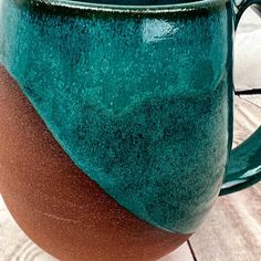 a green and brown coffee mug sitting on top of a tile floor next to a brick wall