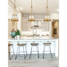 a kitchen island with four stools in front of it and three lights hanging from the ceiling