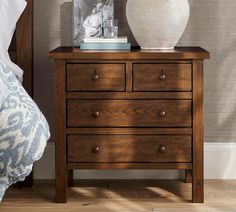 a white vase sitting on top of a wooden dresser next to a lamp and bed