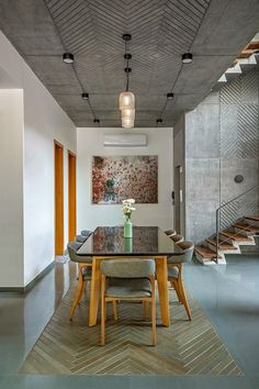 a dining room table with chairs and a painting on the wall behind it in front of stairs