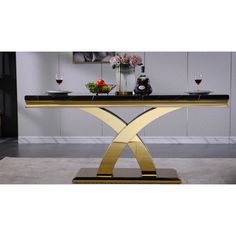 a black and gold console table with two wine glasses on it, in front of a white wall