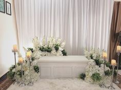 a white bench with flowers and candles on the floor in front of a curtained window