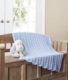 a white teddy bear sitting on top of a wooden bench next to a blue crocheted blanket