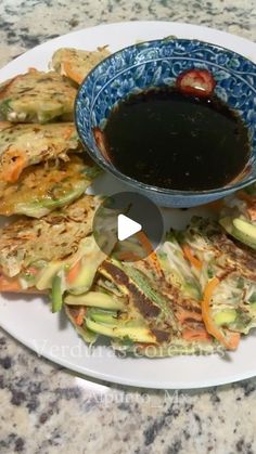 a white plate topped with food next to a bowl of dipping sauce on top of it